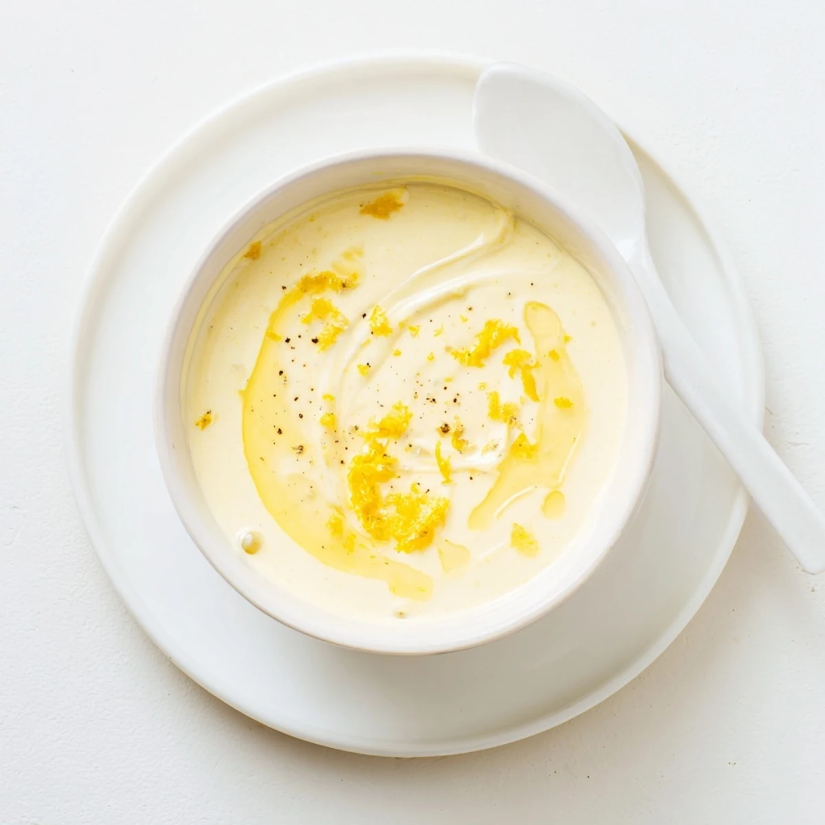 Golden creamy lemon vinaigrette dressing drizzled over fresh mixed greens in white bowl