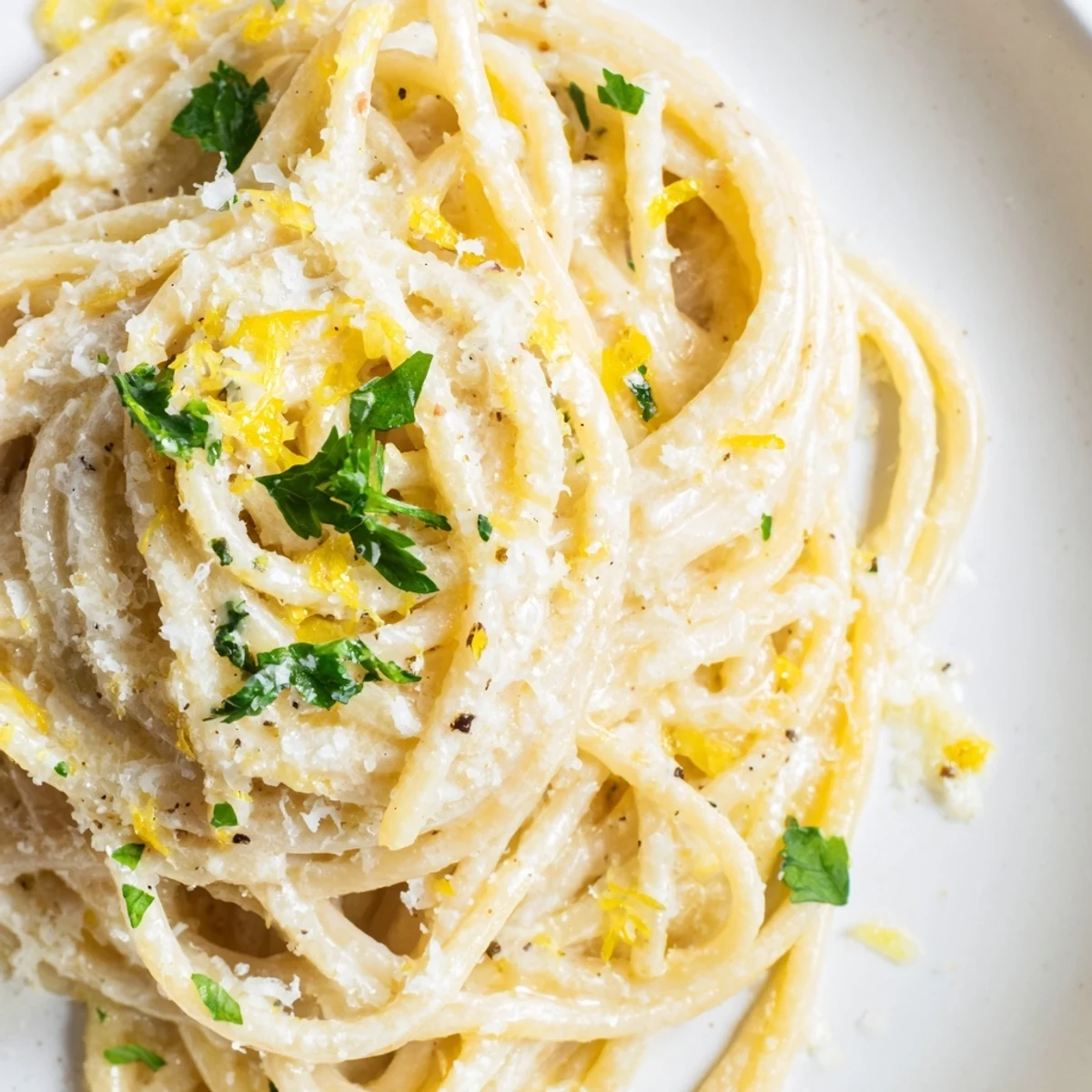 Golden spaghetti coated in rich Parmesan lemon sauce served in a white ceramic bowl