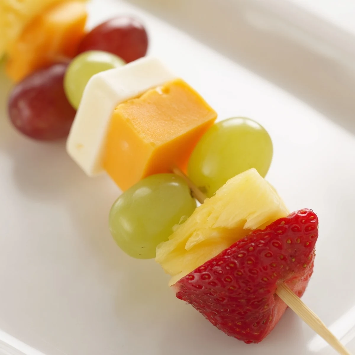 Colorful fruit and cheese kabobs arranged on wooden skewers with fresh mint garnish