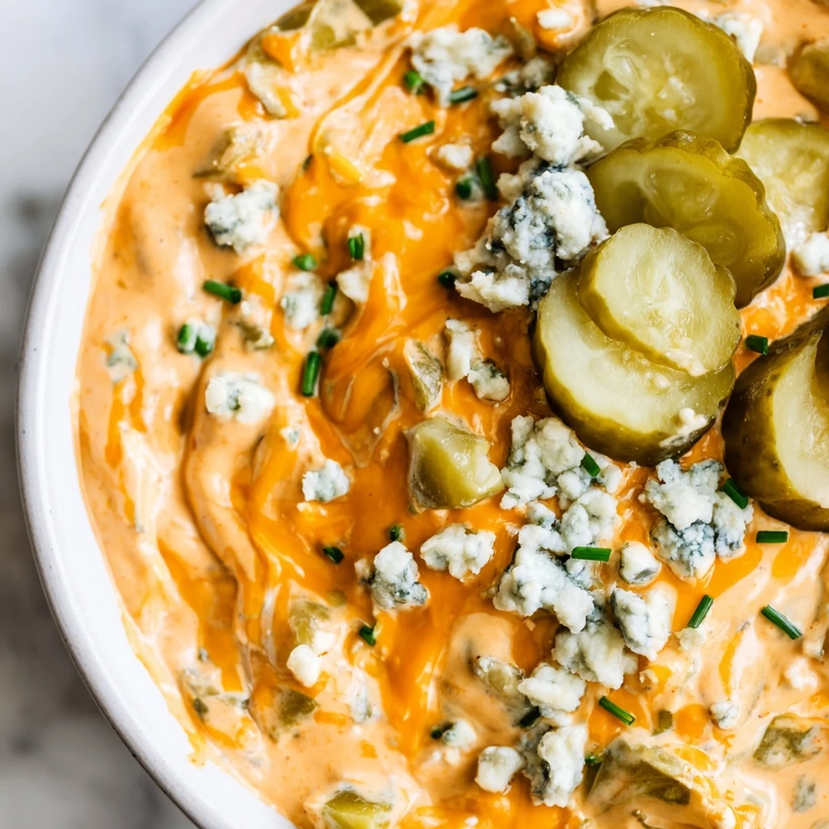 Creamy buffalo pickle dip in a serving bowl surrounded by crispy chips and fresh veggie sticks