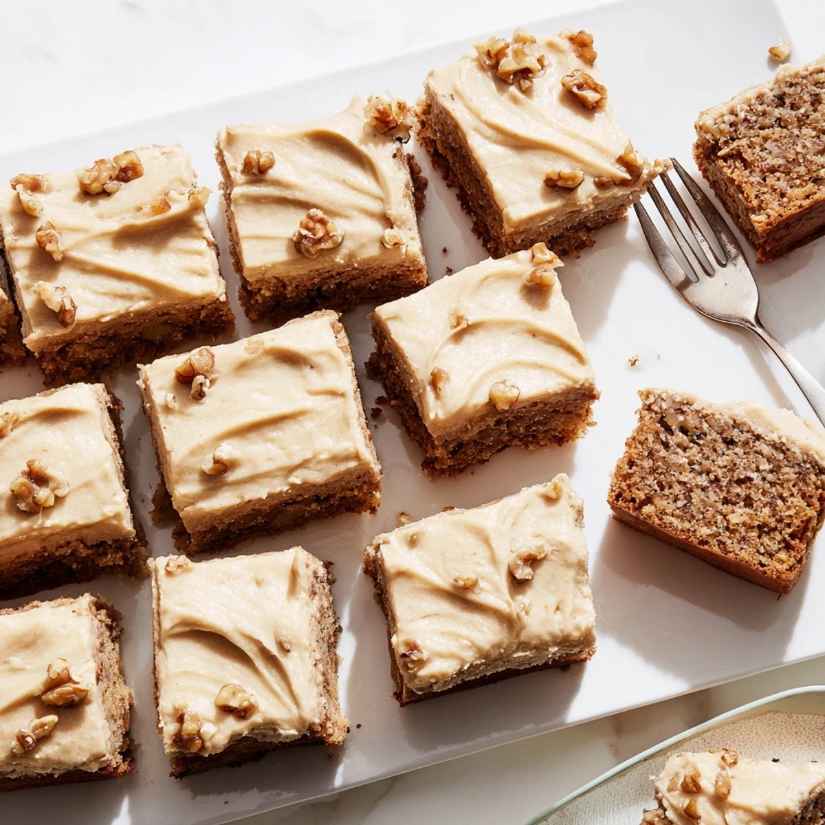 Thick banana bread brownies topped with creamy brown butter frosting on a white plate