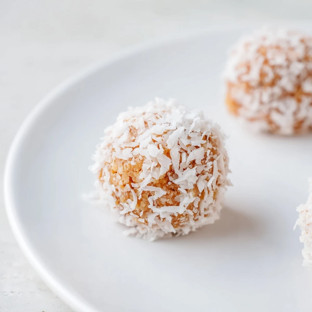 Golden no-bake Citrus Bliss Bites rolled in coconut on a white serving tray