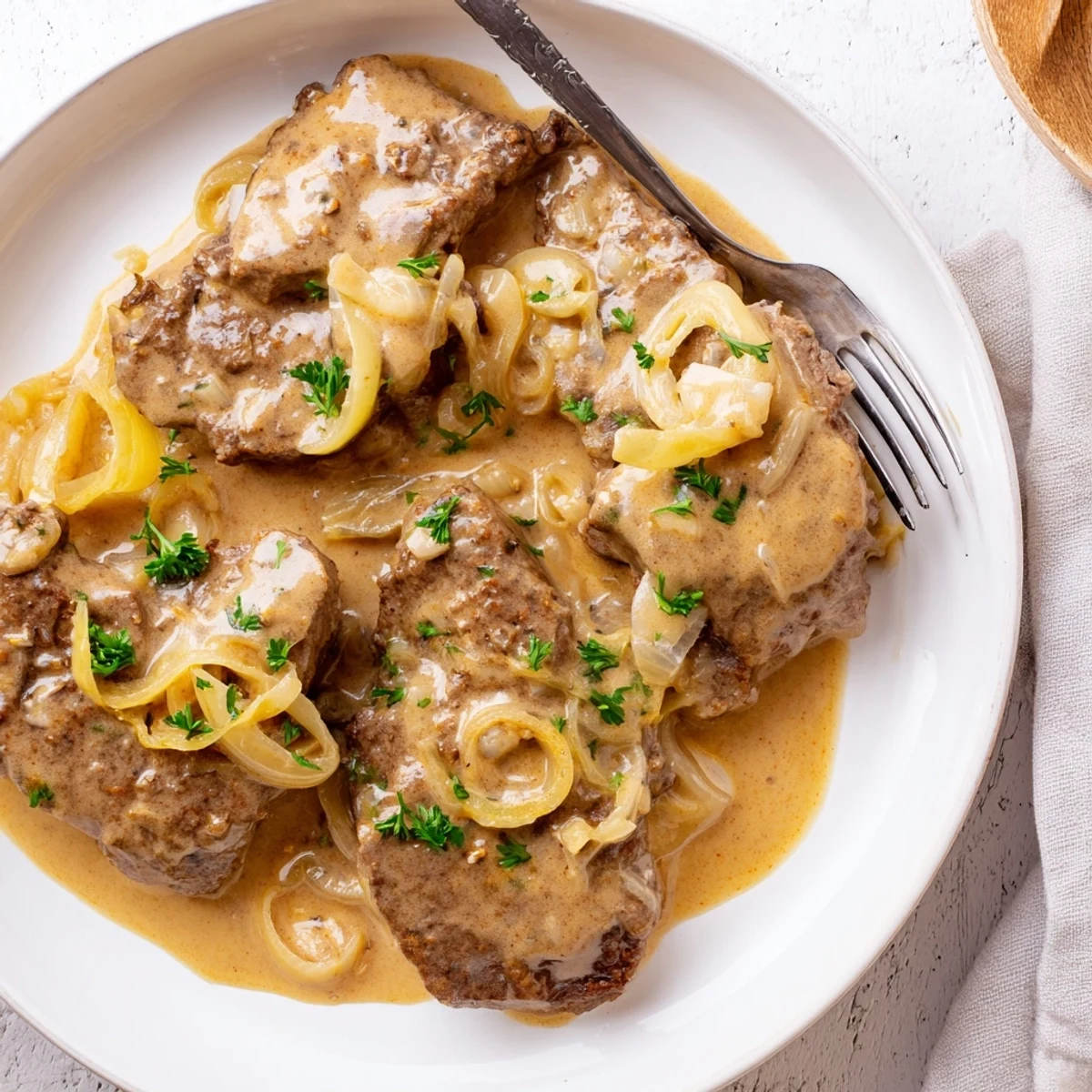Tender Southern style cube steak simmering in thick beef and onion gravy with fresh parsley garnish