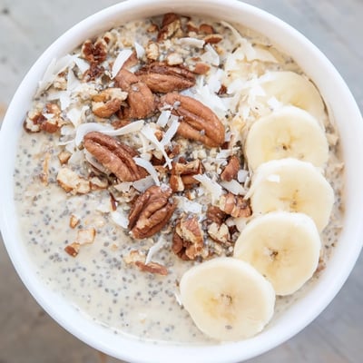 Rich and thick coconut cream pie overnight oats served chilled with banana slices and shredded coconut