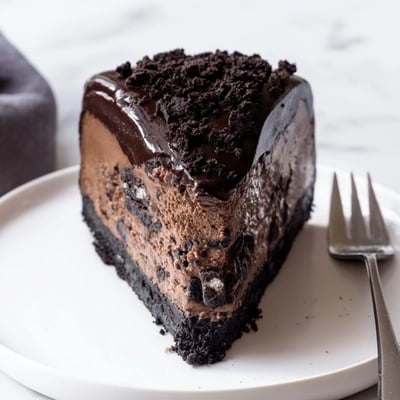 Rich Oreo chocolate cheesecake sliced to reveal a fudgy filling and chocolate drizzle